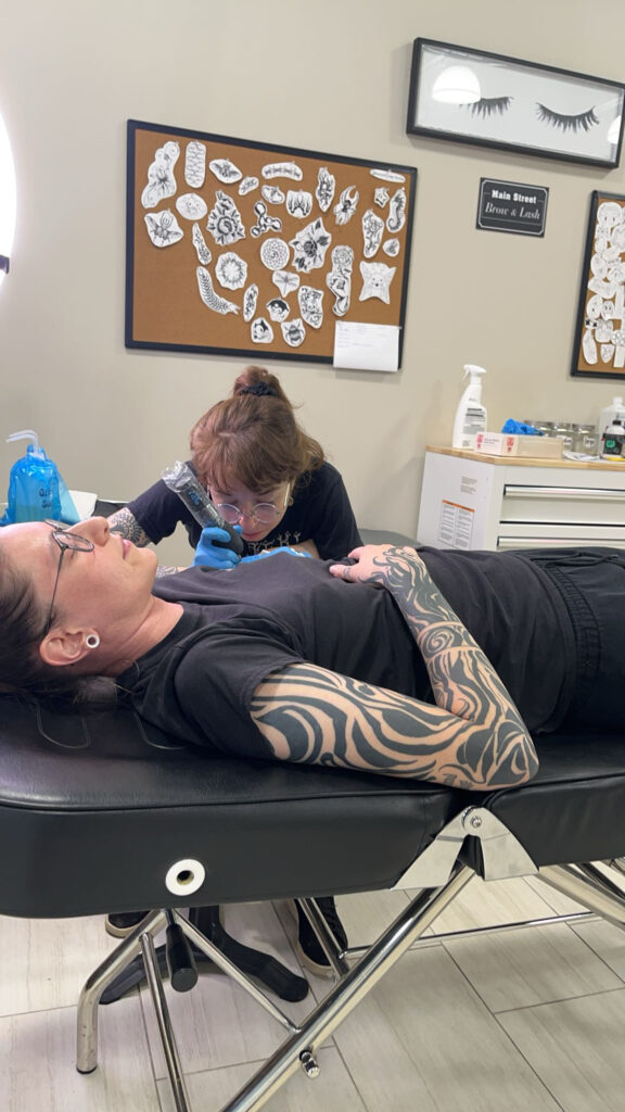 A woman with tattoos is getting her arm worked on by another person.